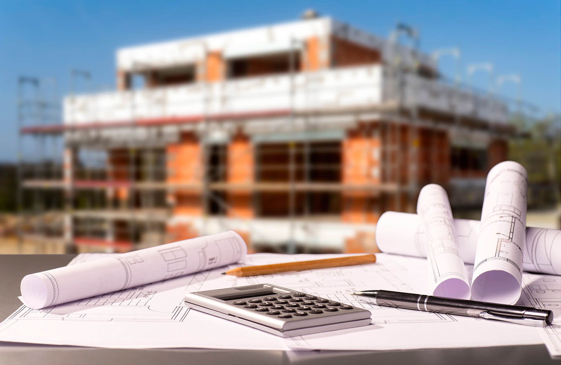 Man sieht Baupläne und darauf liegen zwei Stifte und ein Taschenrechner